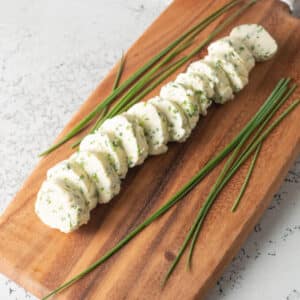 Sliced chive butter on wooden cutting board.