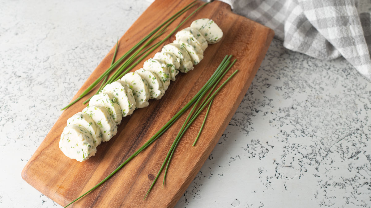 Sliced log of chive butter on a wooden cutting board.