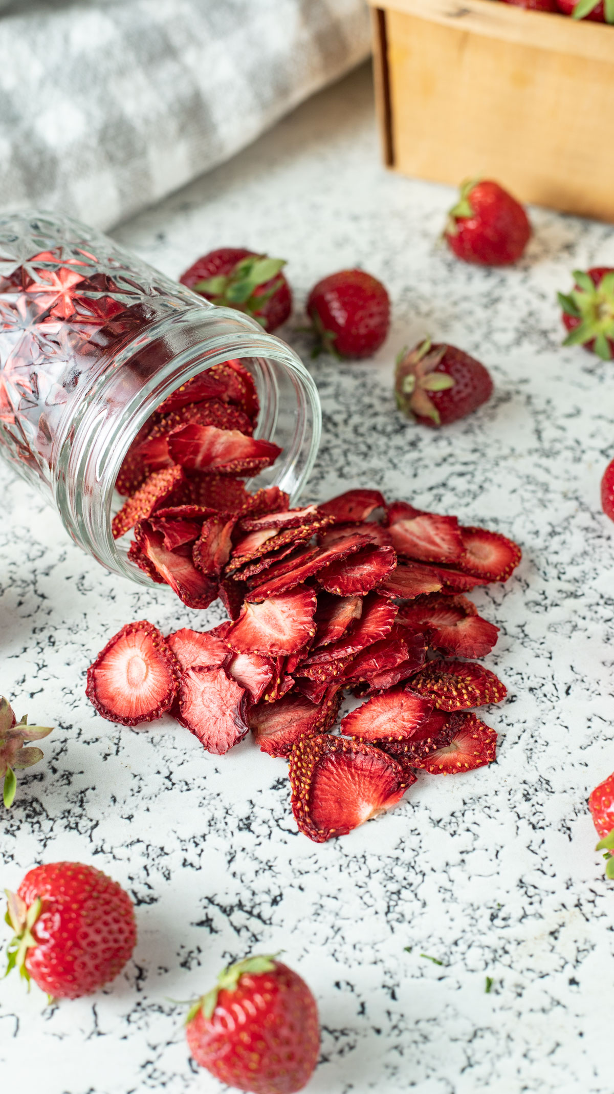 Dried strawberries spilling from a jar with fresh strawberry garnish.
