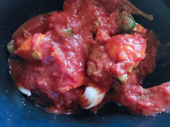 Tomatoes poured over top of the rabbit in slow cooker.