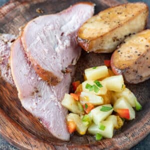 Sliced pheasant breast on round wooden plate with sides.