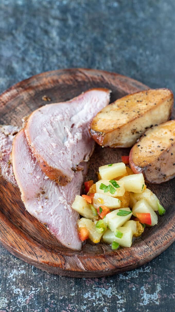 Slices of pheasant breast on wooden plate with colorful citrus salsa.