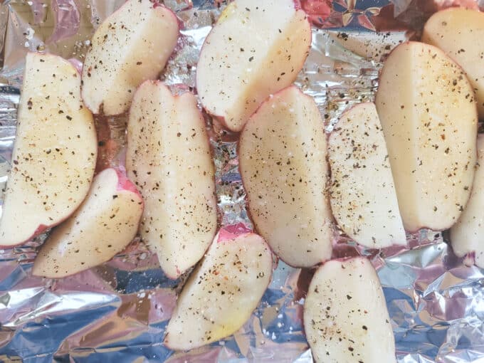 Potato wedges placed on aluminum foil and rubbed with olive oil and sprinkled with seasonings