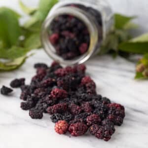 Dried blackberries on marble board with fresh leaves.