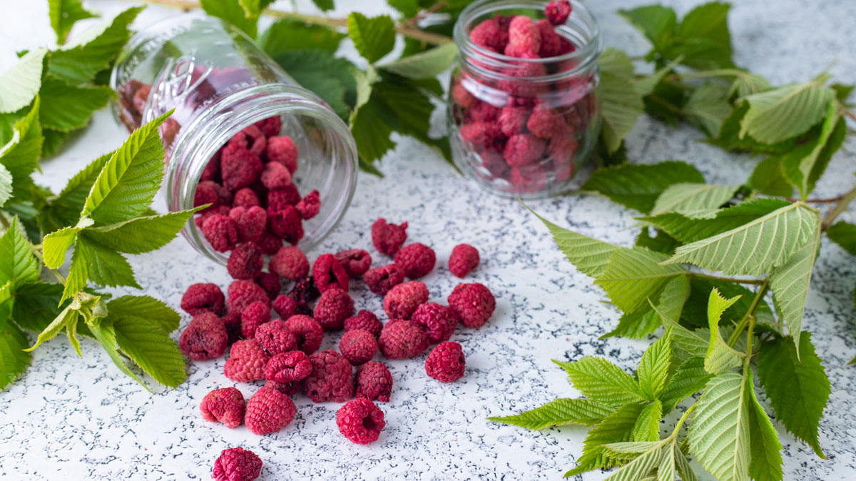 Dried raspberries with raspberry leaves on white board.