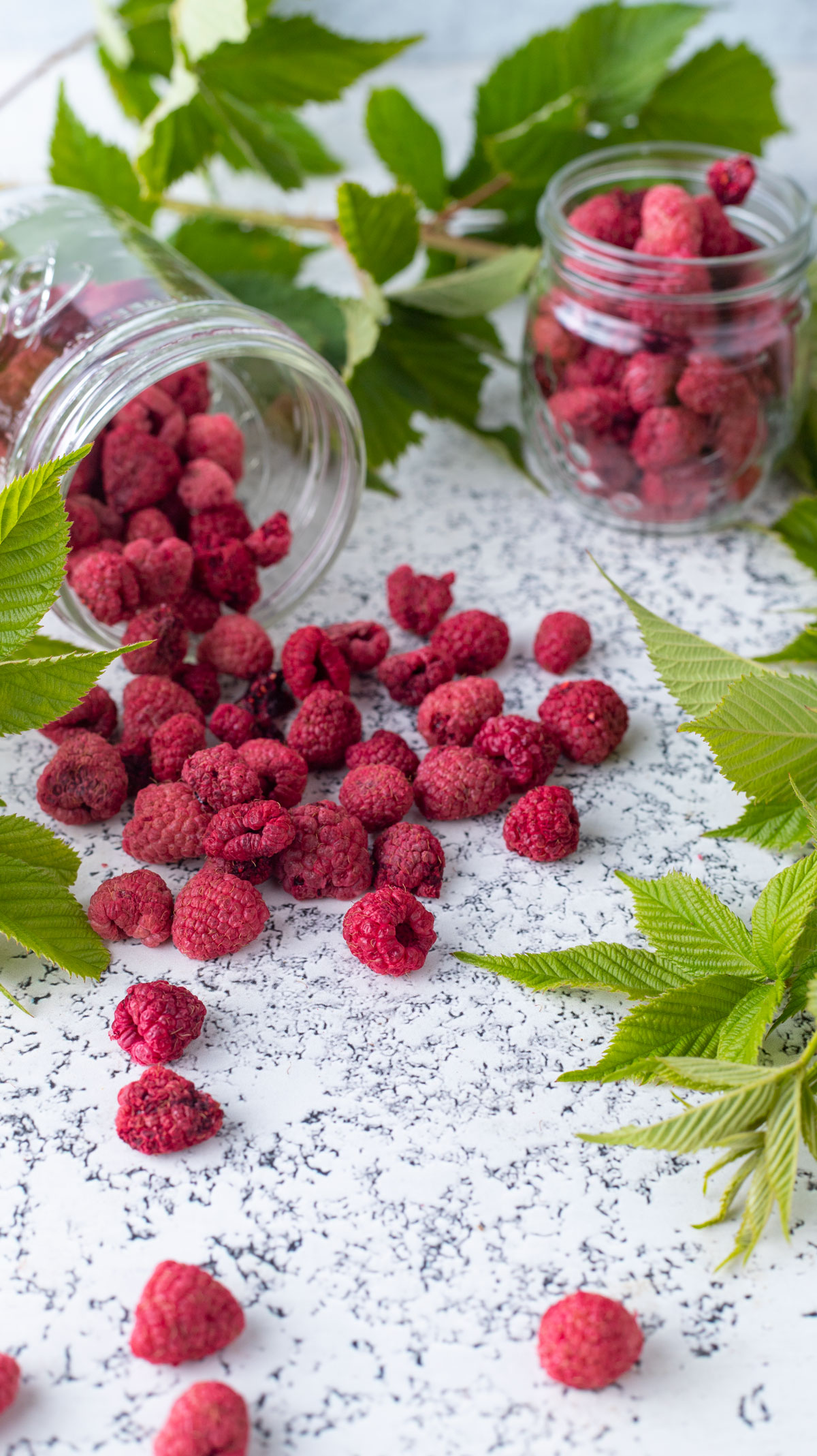 Raspberries spilling out of pint jar onto light background.