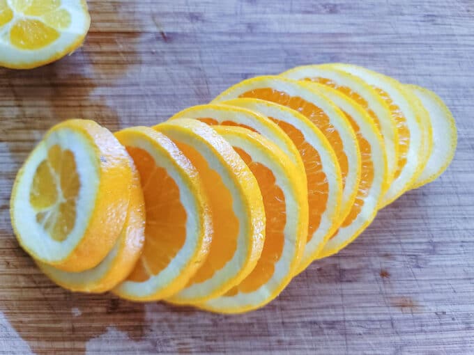 Row of sliced orange slices on wooden cutting board.