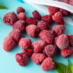 Frozen raspberries on teal board.