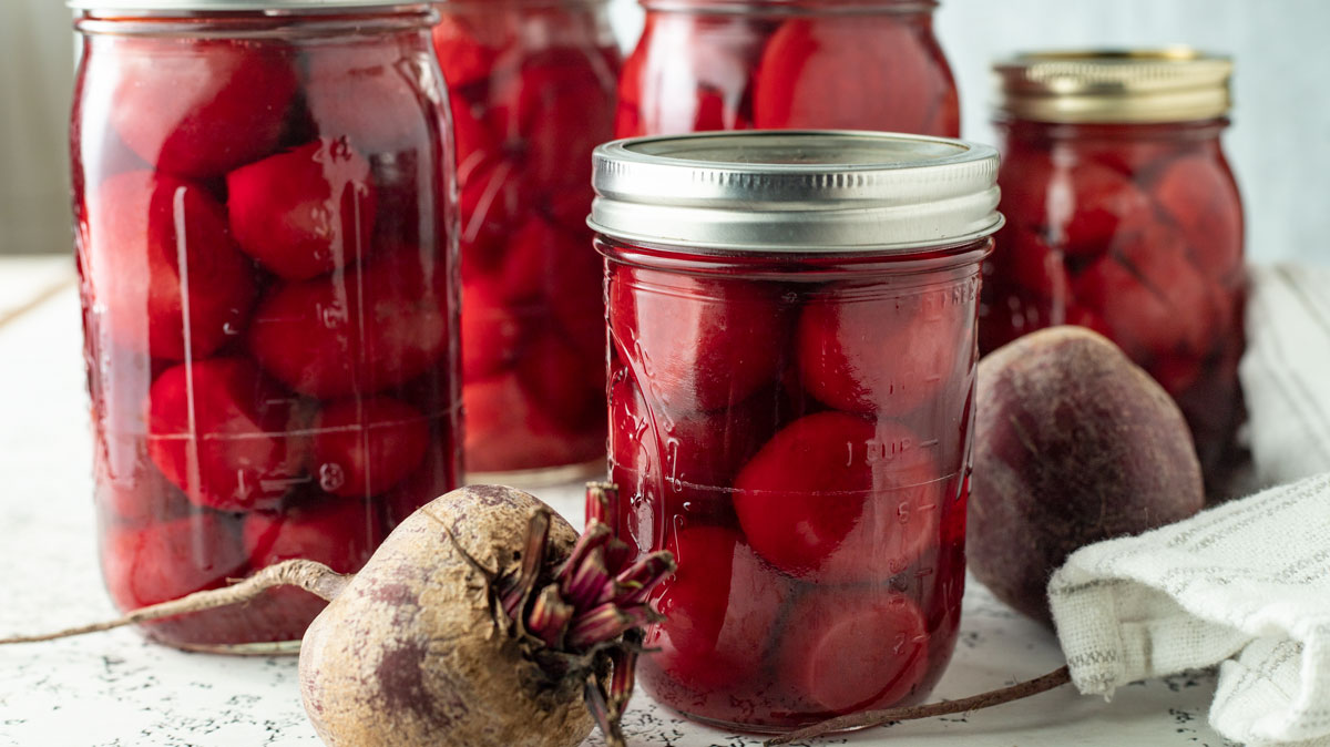 Jars of whole and sliced beets on a white background.
