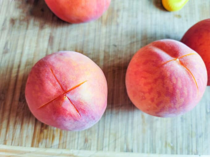 Peaches on cutting board with x scored into bud end.