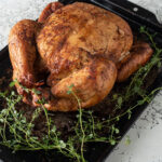 Whole browned chicken on a blackened metal tray.