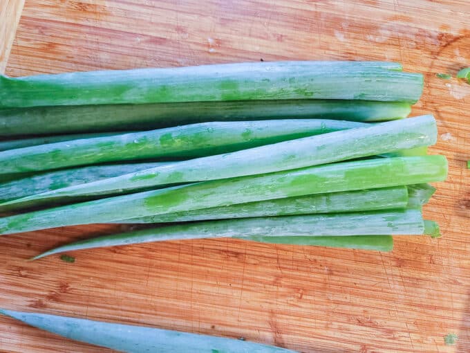 Pile of washed scallions on cutting board.