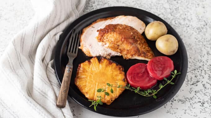 Black plate with chicken, beets, potatoes and pineapple.