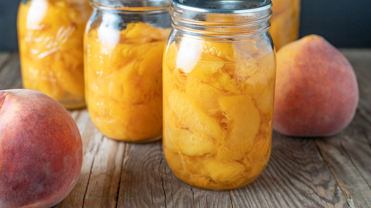 Jars of sliced peaches on a wooden board.
