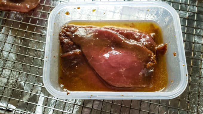 Venison slices in marinade in plastic container.