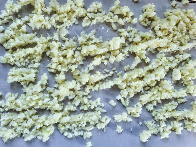 Minced garlic spread out on lined dehydrator rack. 
