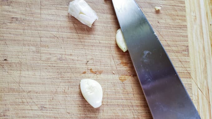Crushing garlic with the side of a chef's knife.