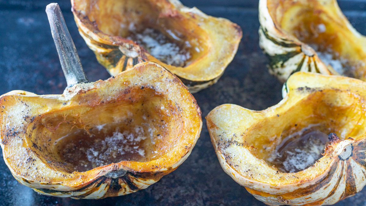 Four halved cooked squash on black tray.