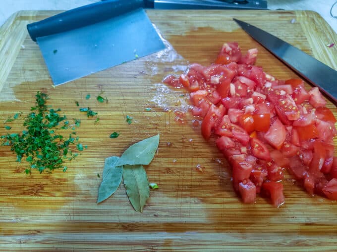 Chopped tomatoes, thyme and bay leaf on cutting board.