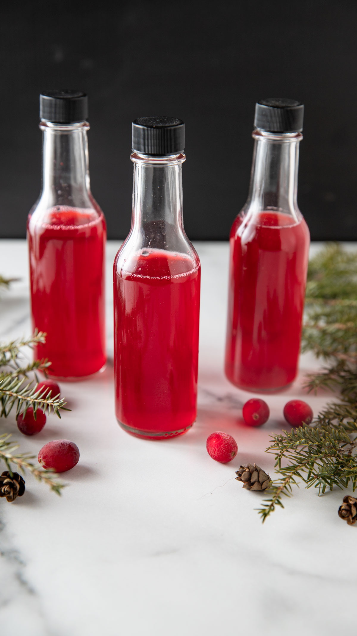 Jars of vinegar with greens and fresh cranberries.