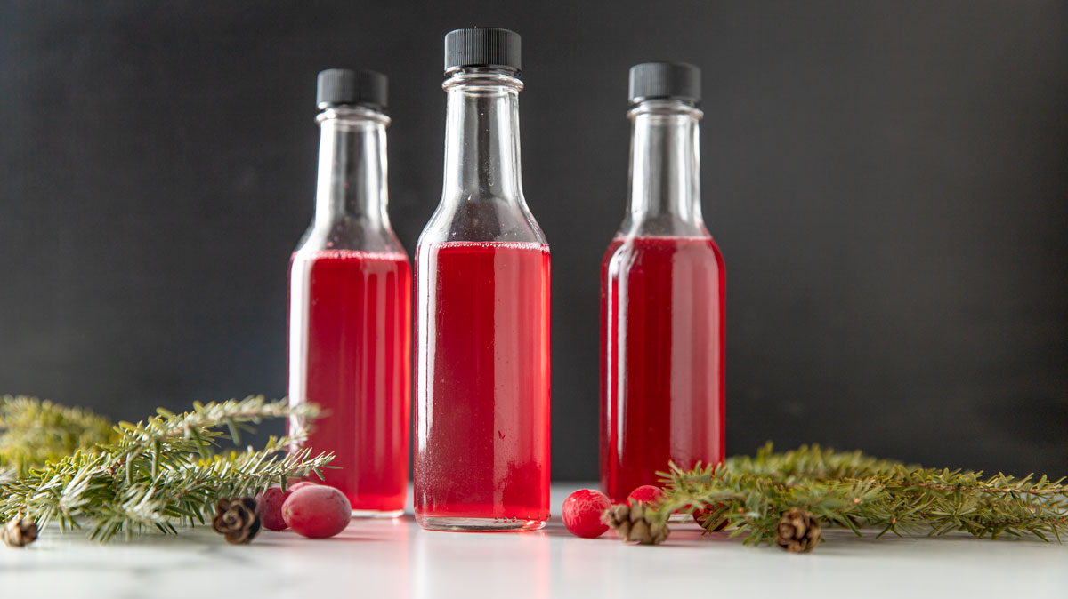 Jars of vinegar with greens and fresh cranberries.