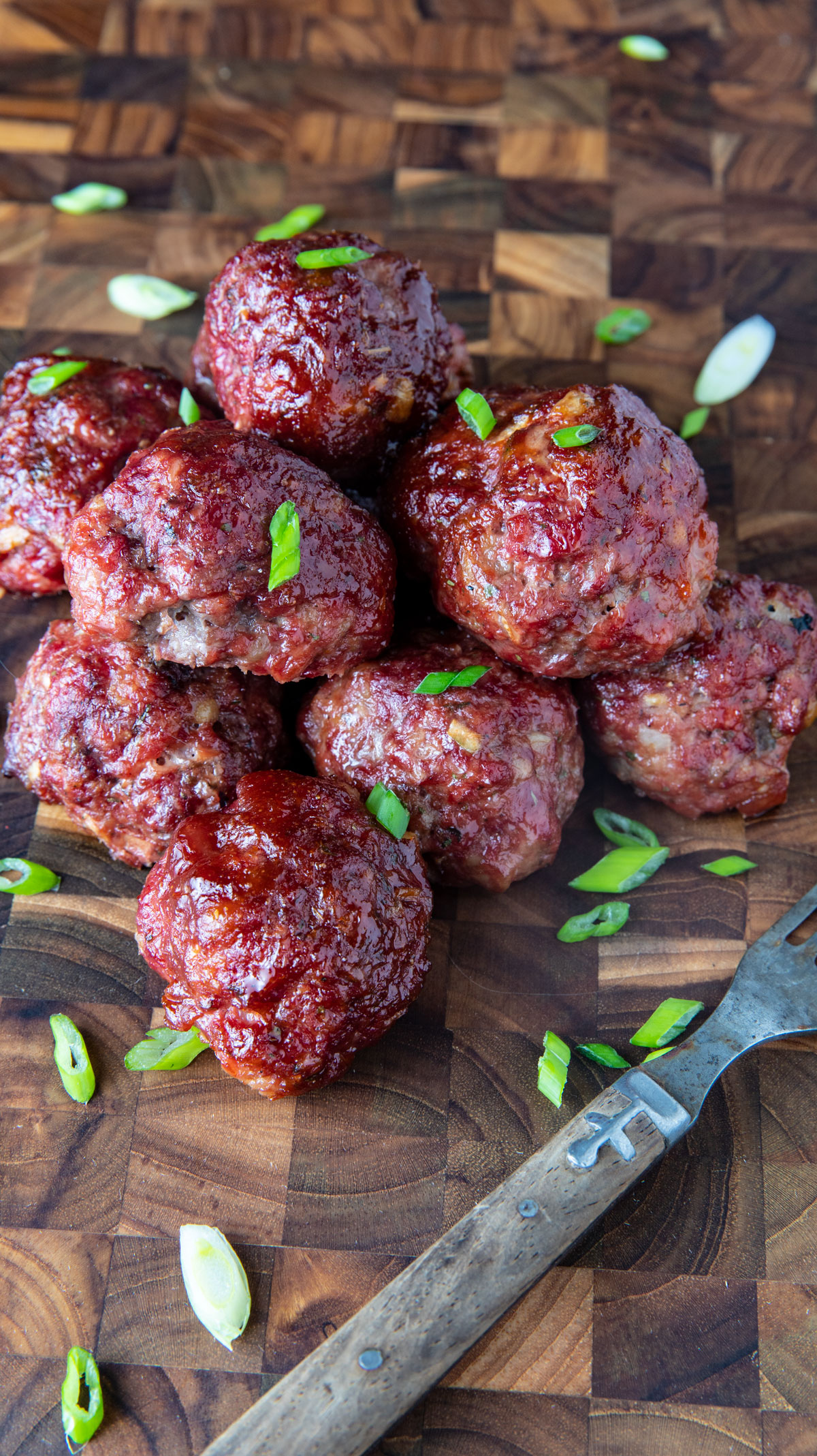 Meatballs piiled on a cutting board and garnished with sliced green onion.