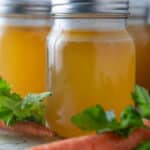 Jars of chicken stock with fresh vegetables in front.