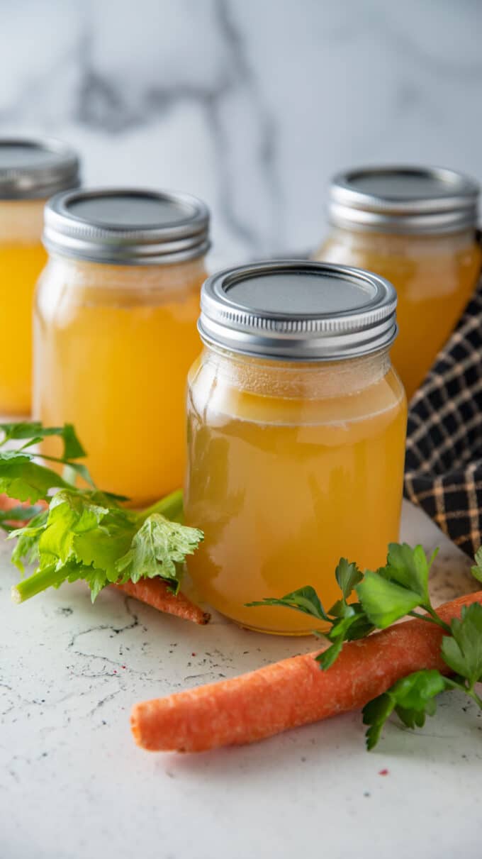 Four jars of stock on a white board with fresh aromatics.