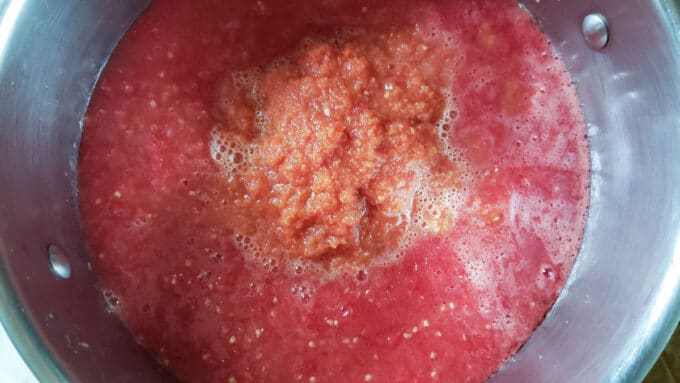 Vegetables added to tomatoes in pot.