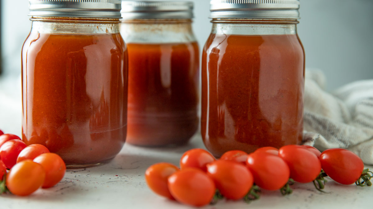 Tomato soup jars with fresh tomatoes on the side.