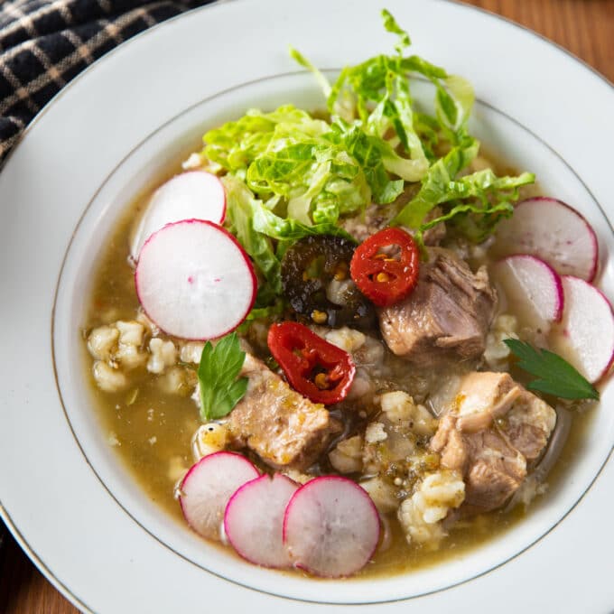 Bowl of pork pozole verde with colorful condiments.