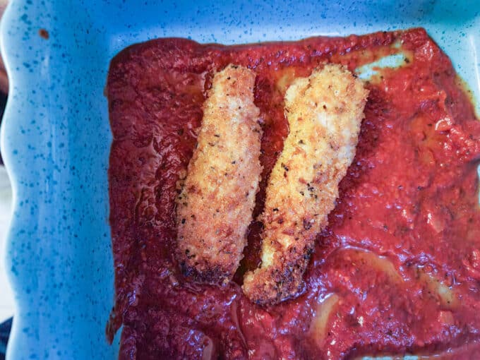 Rabbit loins laid on top of sauce in a casserole dish.