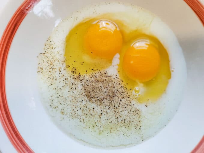 Two eggs in a bowl with milk and spices.