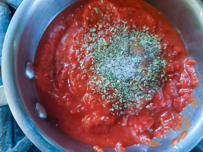 Seasonings added to tomato sauce in a pot.
