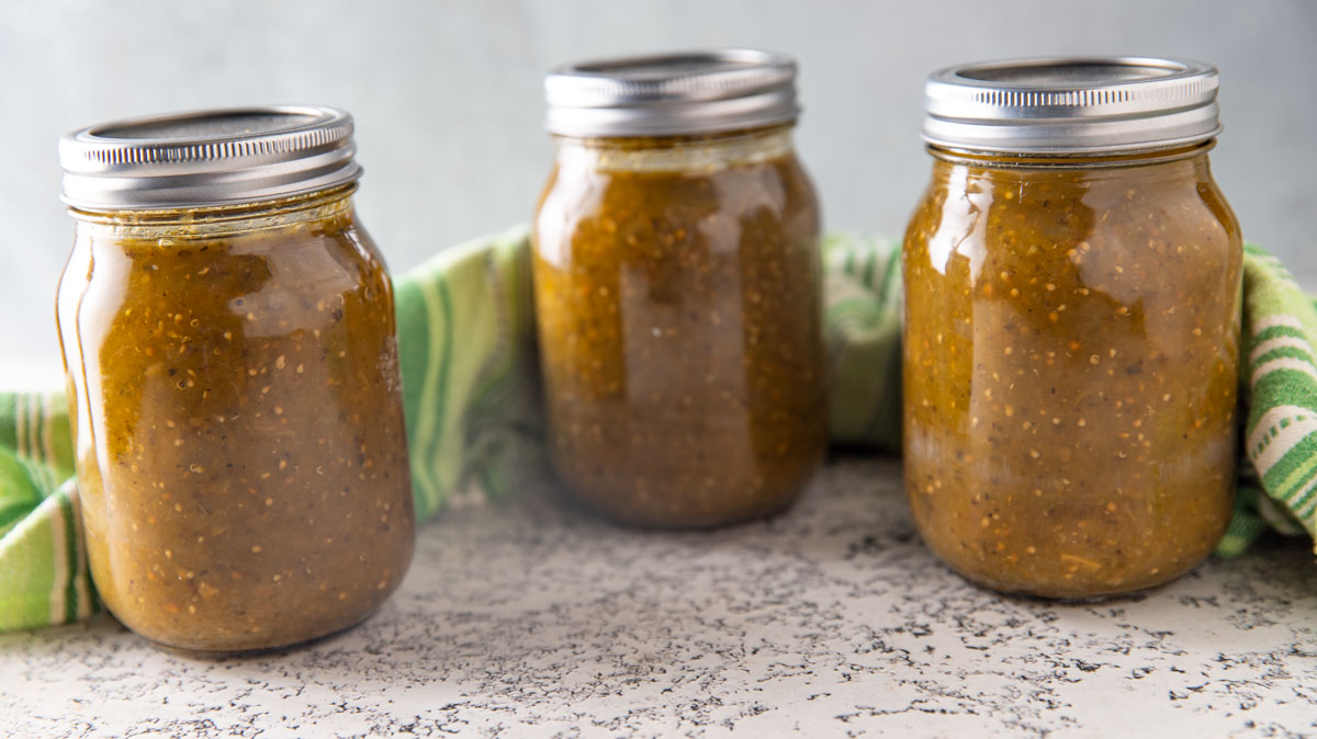 Three jars of green tomato sauce on white board.
