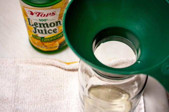 Canning jar with canning funnel next to a bottle of lemon juice.