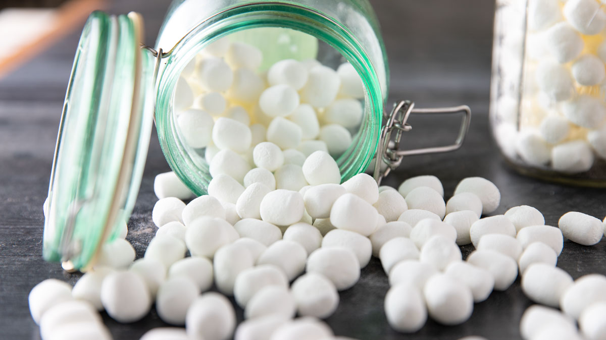 Marshmallows spilling out of a green storage jar onto a black board.