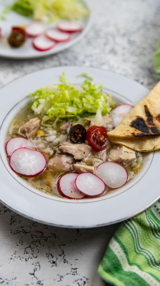 Colorful chicken pozole in a white bowl.