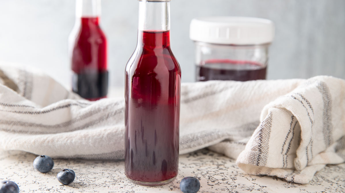Bottles of blueberry vinegar with blueberries on a white board.