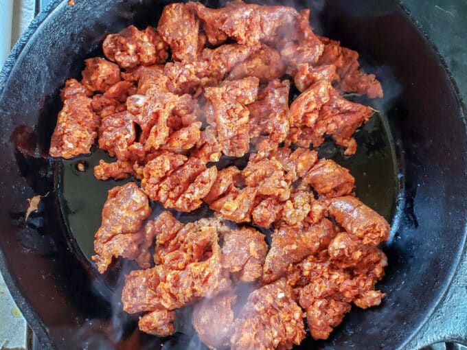 Raw chorizo broken up and added to a frying pan.