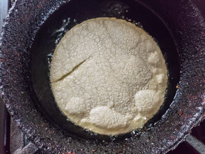 Corn tortillas added to hot oil in a frying pan.