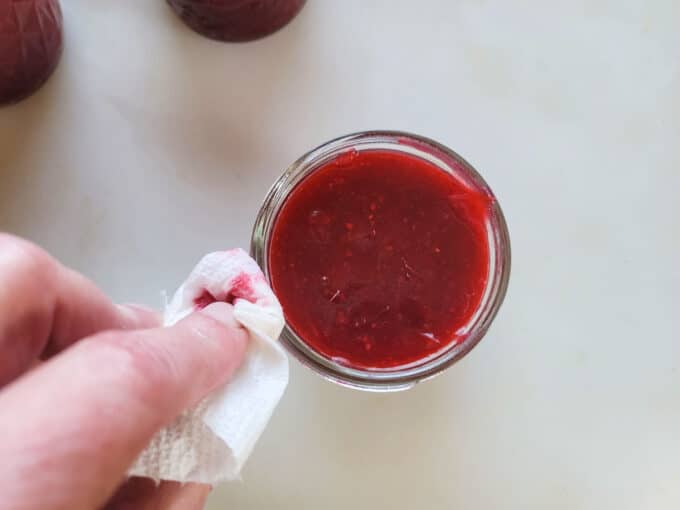 Wiping the jar rim with a paper towel.
