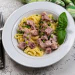 Pasta with peas and ham in a white bowl garnished with fresh basil.