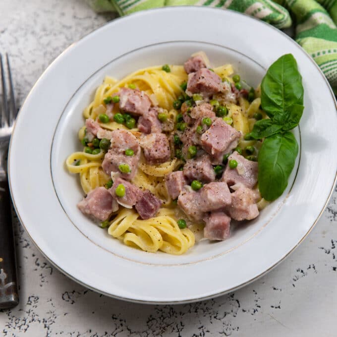Pasta with peas and ham in a white bowl garnished with fresh basil.