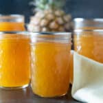 Half-pint jars of pineapple jam in front of a whole pineapple.