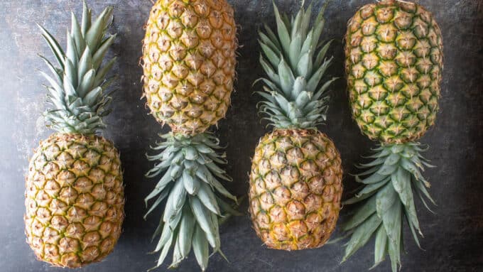 Artistically arranged whole pineapples on a black board.