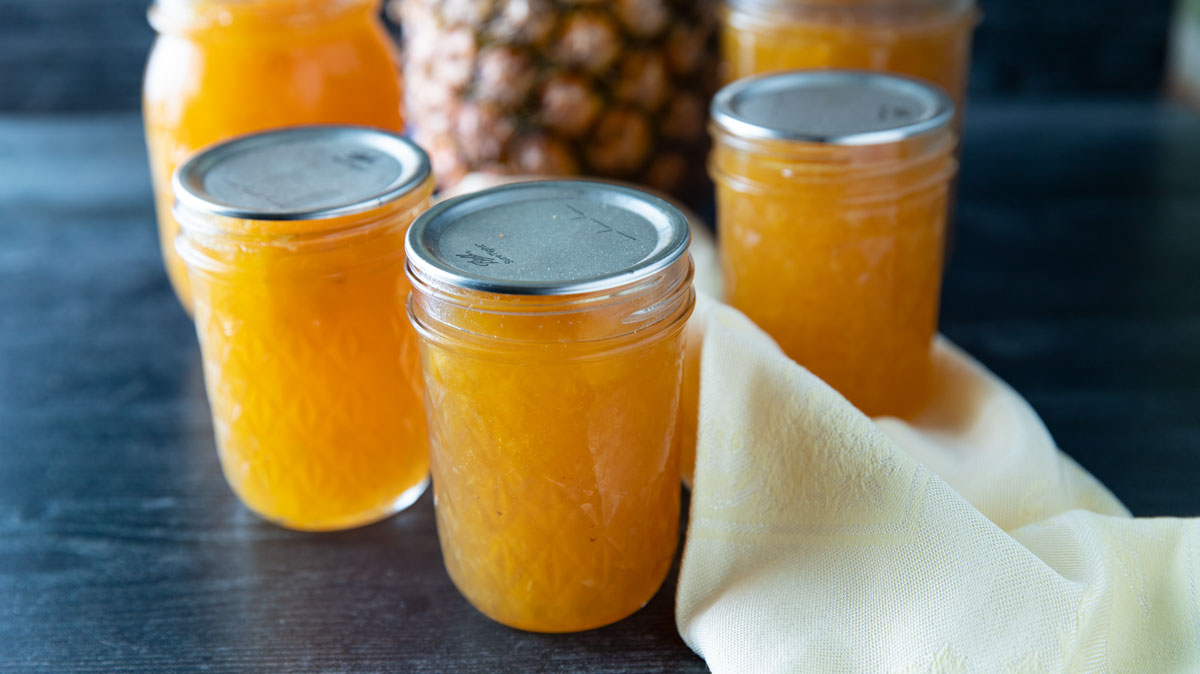 Jars of pineapple jam with a whole pineapple in the background.