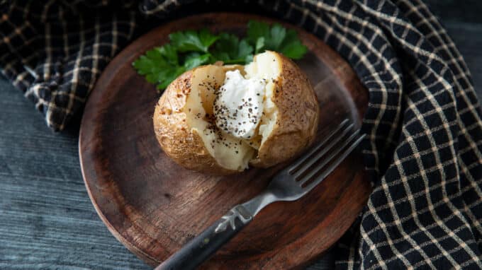Baked potato on a wooden plate with parsley.