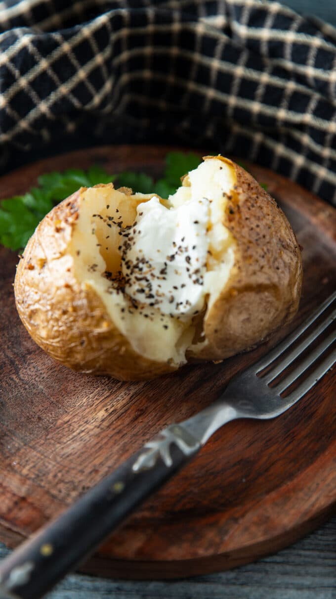 Sour cream topped baked potato on a wooden plate.