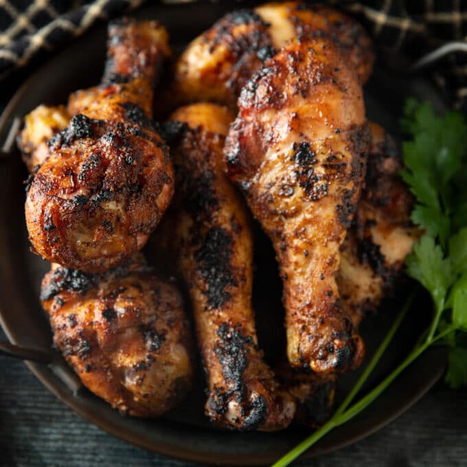 Pile of crispy smoked chicken legs on a black plate.